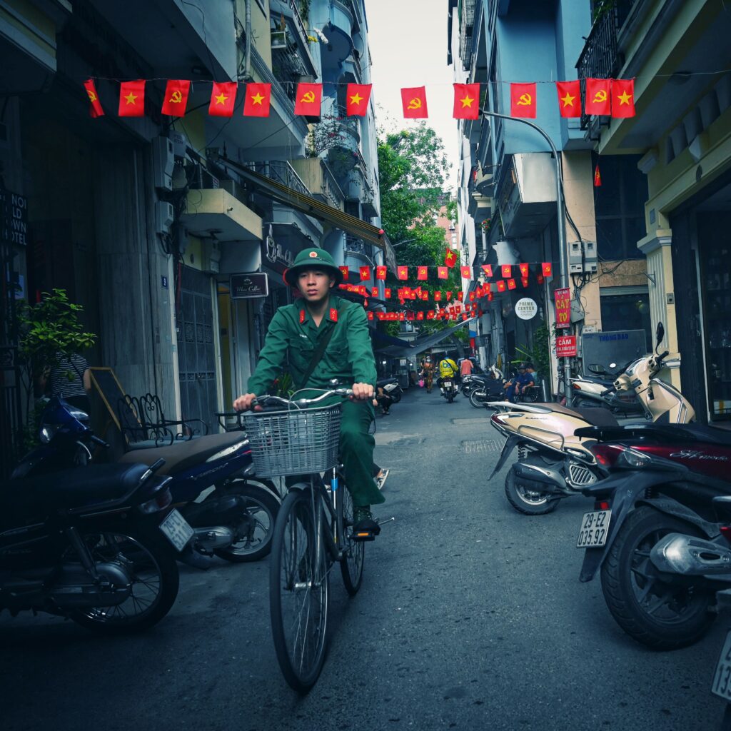 A person on a bicycle in a narrow street adorned with Vietnamese flags in Hanoi.