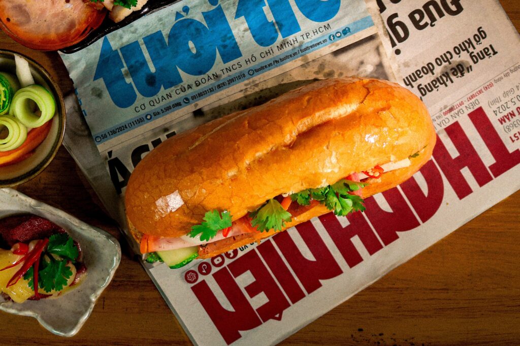 Traditional Vietnamese bánh mì sandwich placed on local newspaper, surrounded by fresh ingredients, offering a cultural and gastronomic glimpse of Việt Nam.