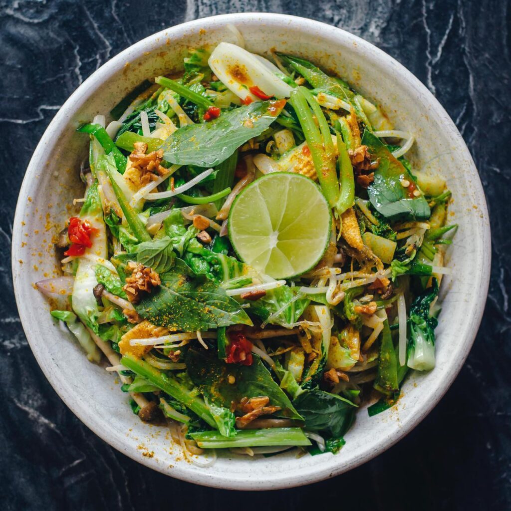 Top view of a vibrant vegan salad with fresh greens and lime in a bowl.
